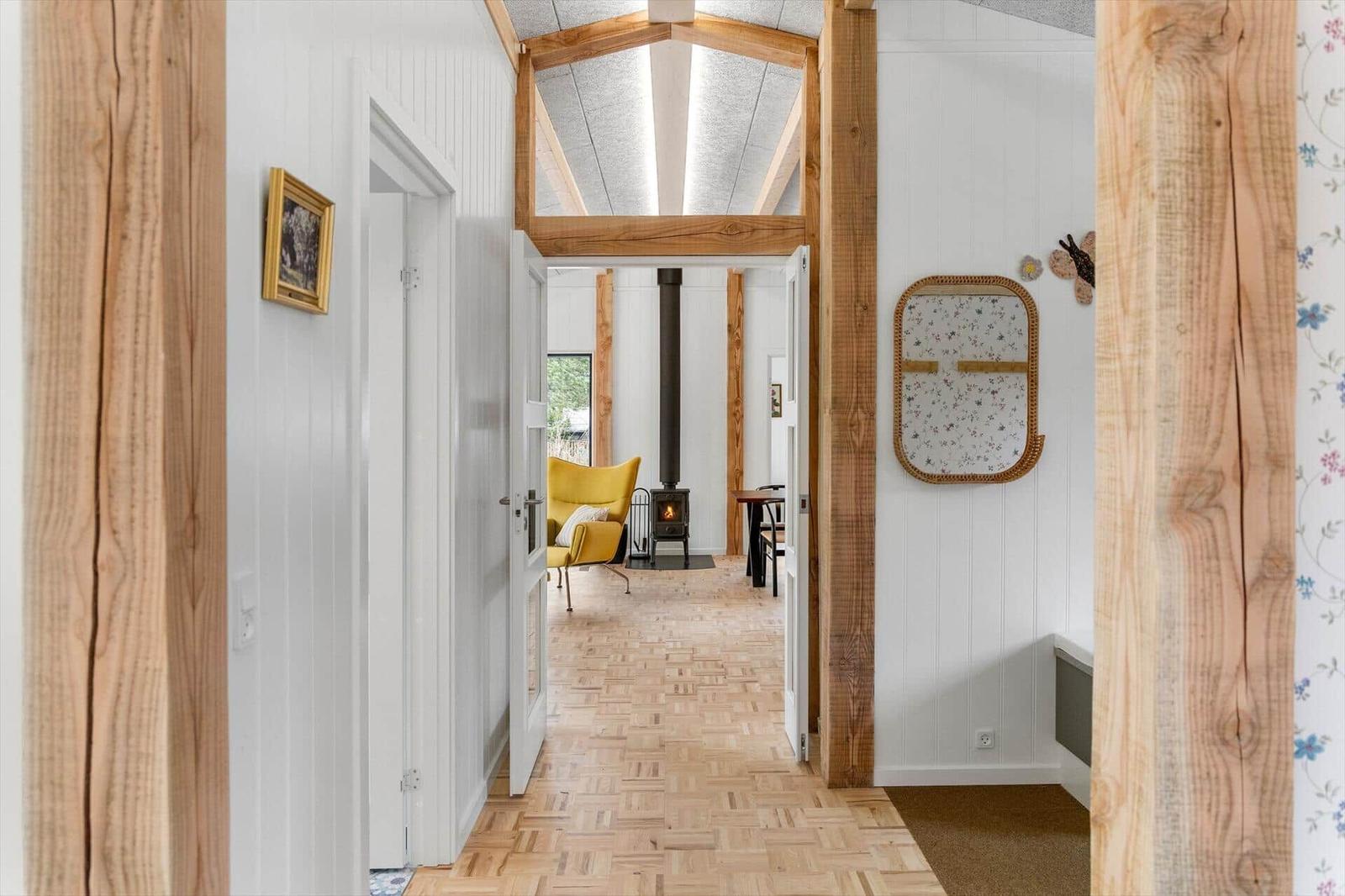 Hallway with wooden floor and beams, view into living area with yellow seating and fireplace.