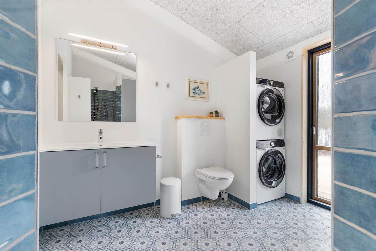Bathroom with washing machine, toilet, and mirror. Blue tiles on walls.