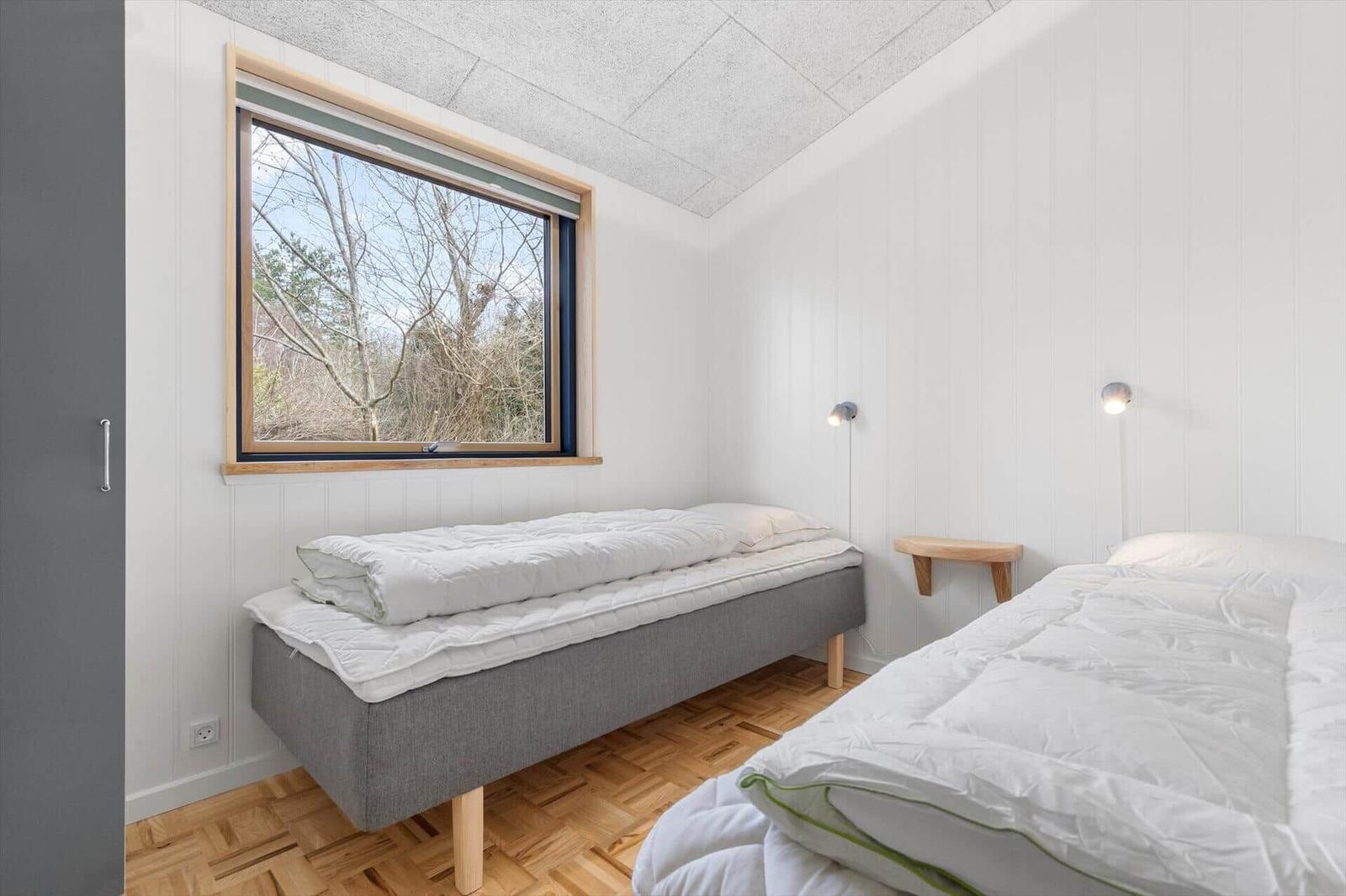 Room with two beds, window view of forest and wooden floor.