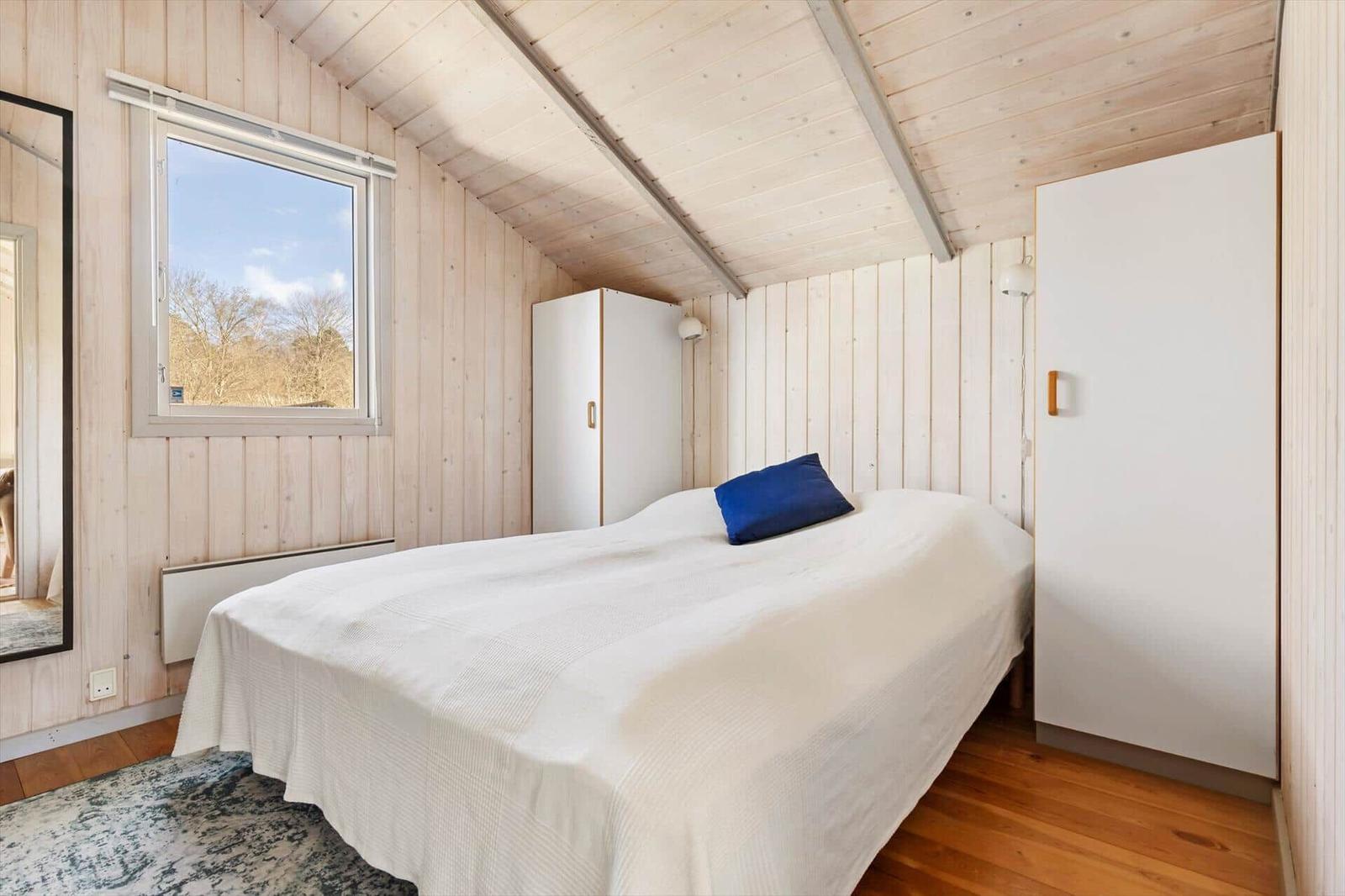 Bedroom with wooden walls, bed, window, and closets.