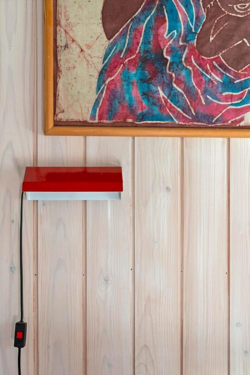 Red wall lamp under framed artwork on wood panel wall