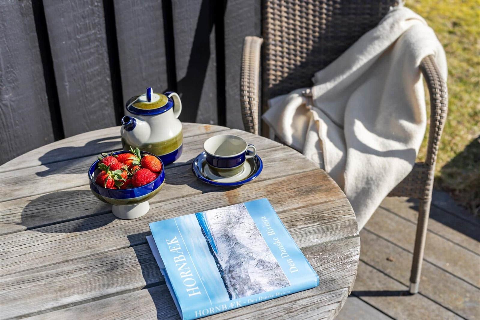 Round table with tea, strawberries, and book on terrace.
