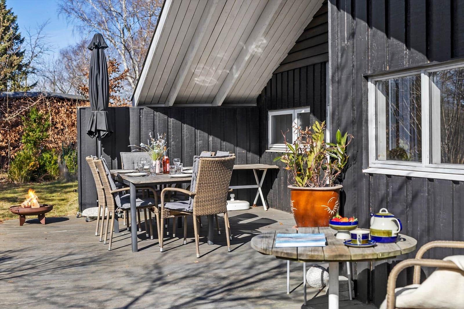 Deck with table, chairs, plants, and fire pit beside dark wooden house.