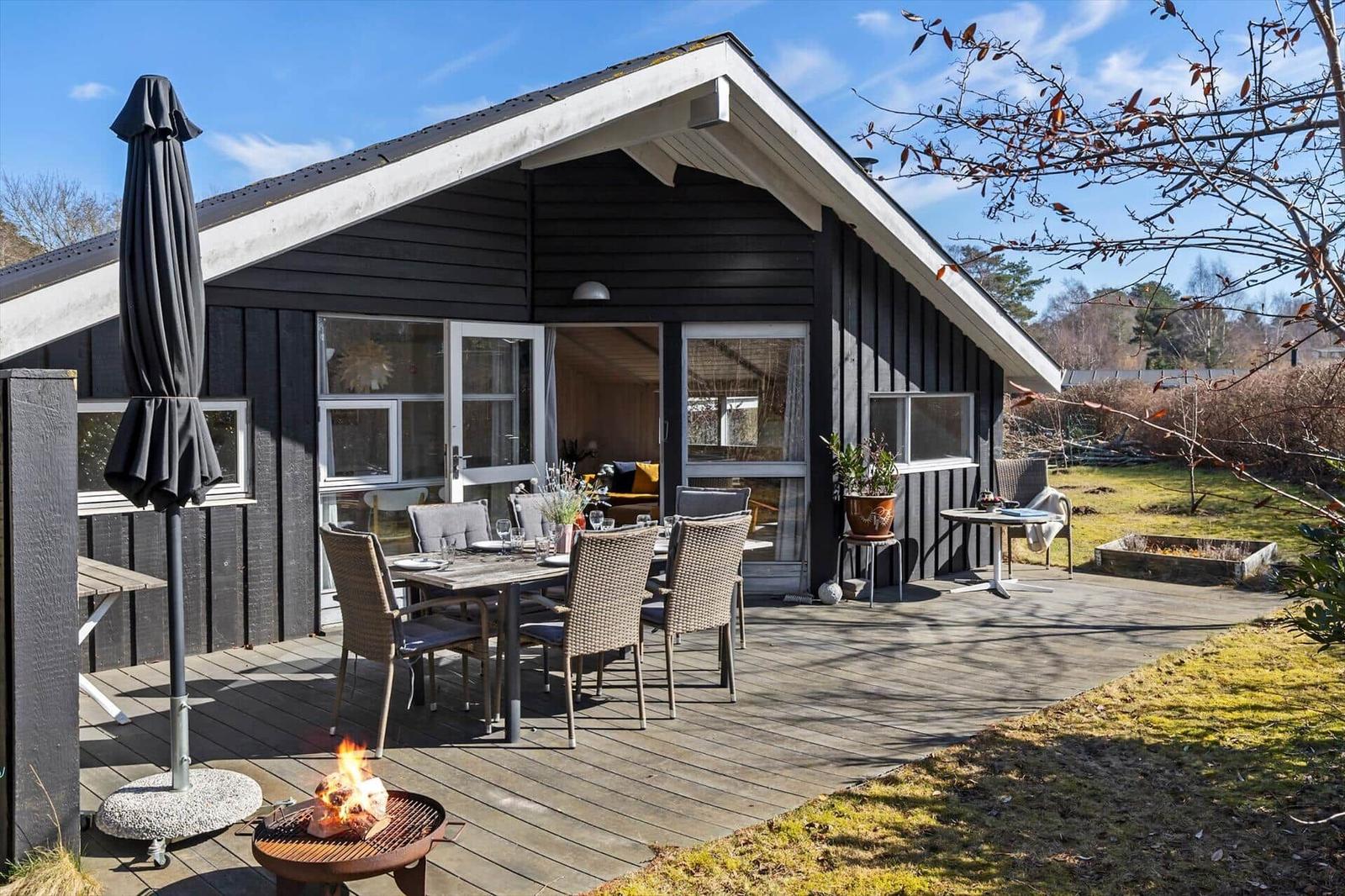 Deck with seating, grill, and closed umbrella in front of a wooden house.