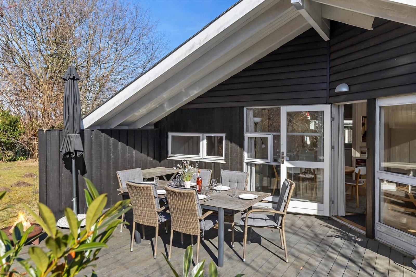 Deck with dining table, chairs, and fire pit in front of a house with sliding door.
