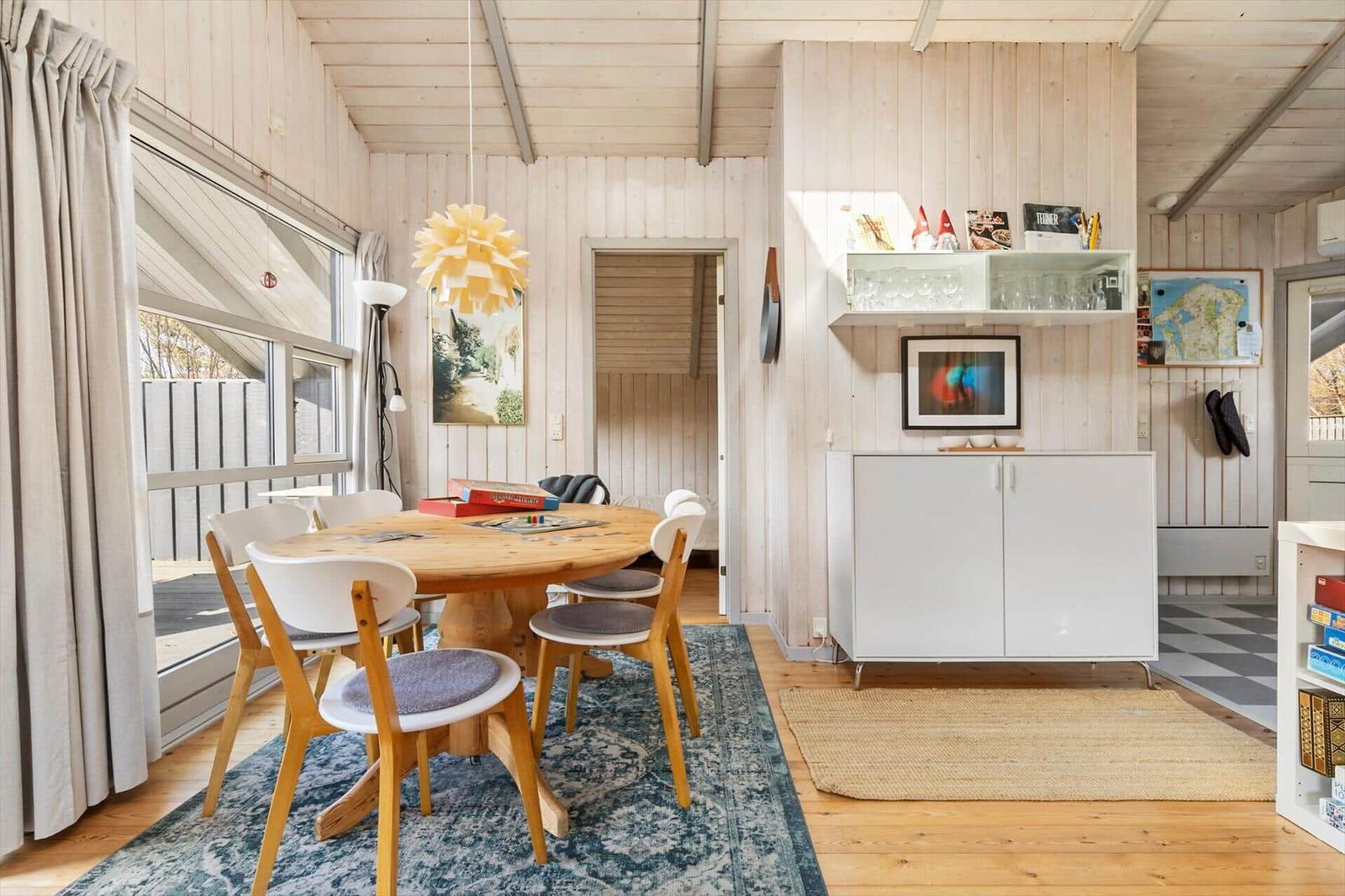 Dining area with round table and chairs, wall shelf and fireplace. Wooden walls and floor.