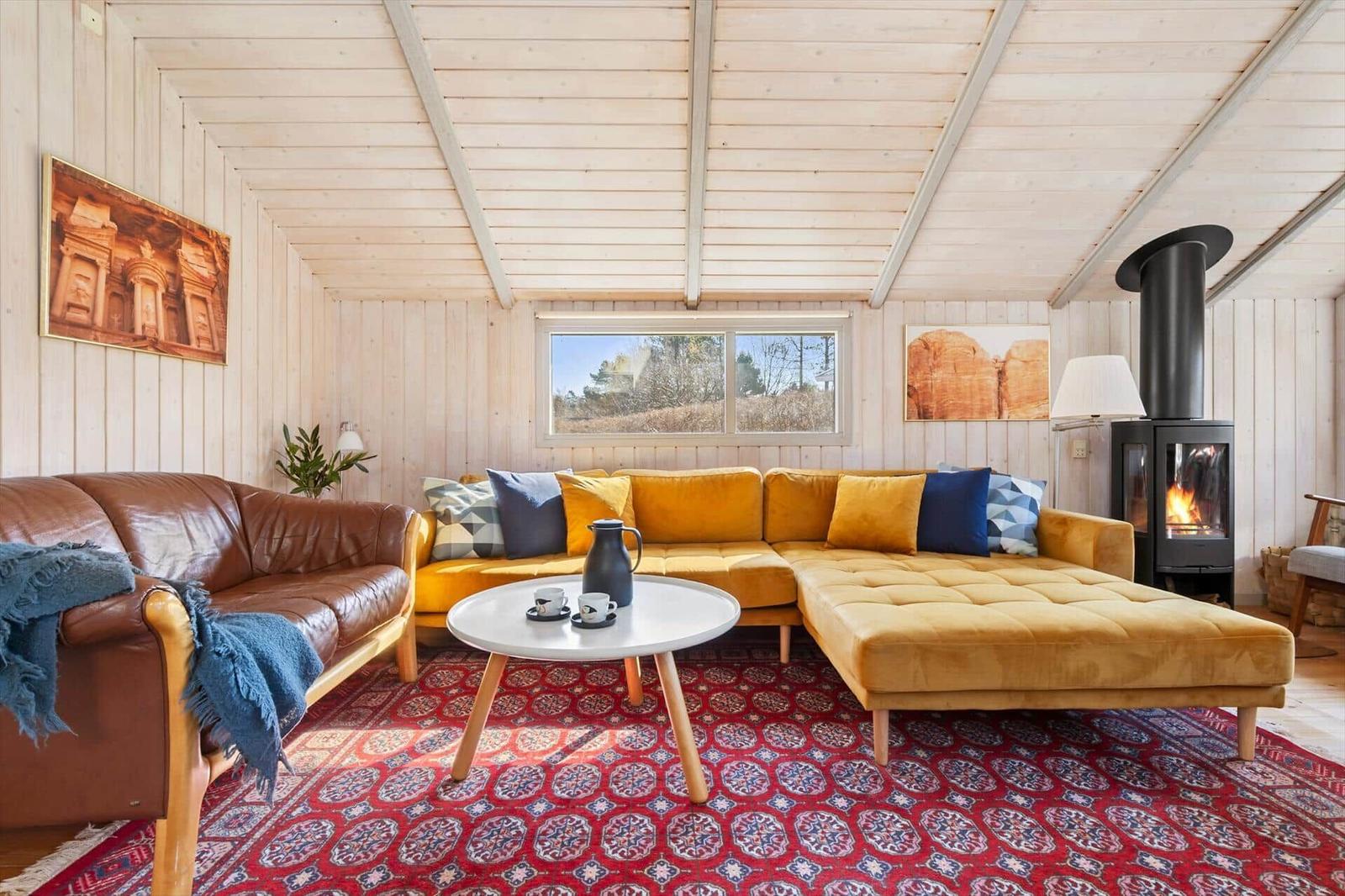 Living room with yellow sofa, wooden ceiling, and wood stove.