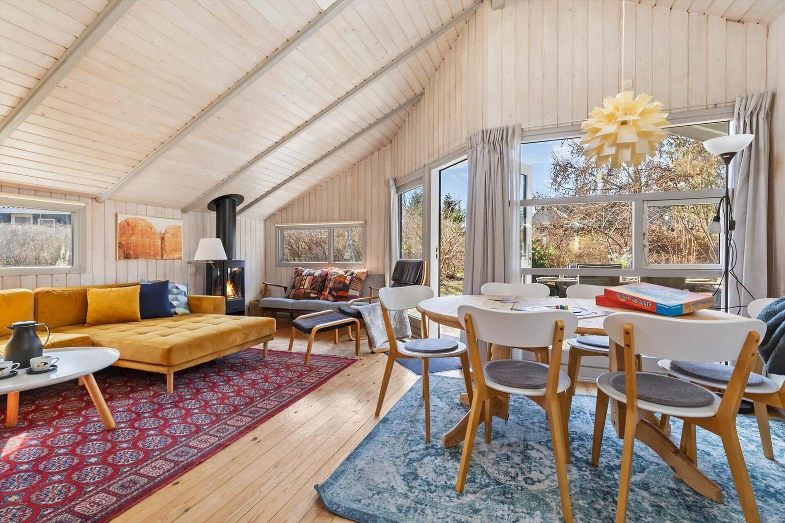 Living and dining area with wooden ceiling, sofa, dining table, and windows.