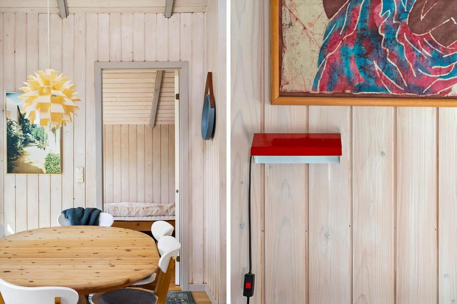 Dining area with round table and white chairs, wall with artwork and red wall lamp.