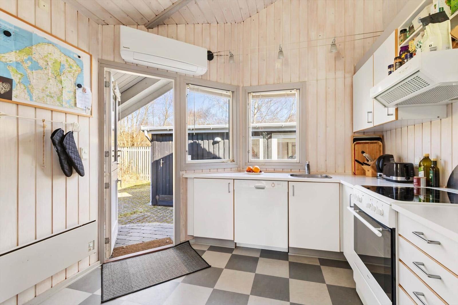 Kitchen with white cabinets, sink, and stove. Wooden walls and tiled floor. Door leads outside.