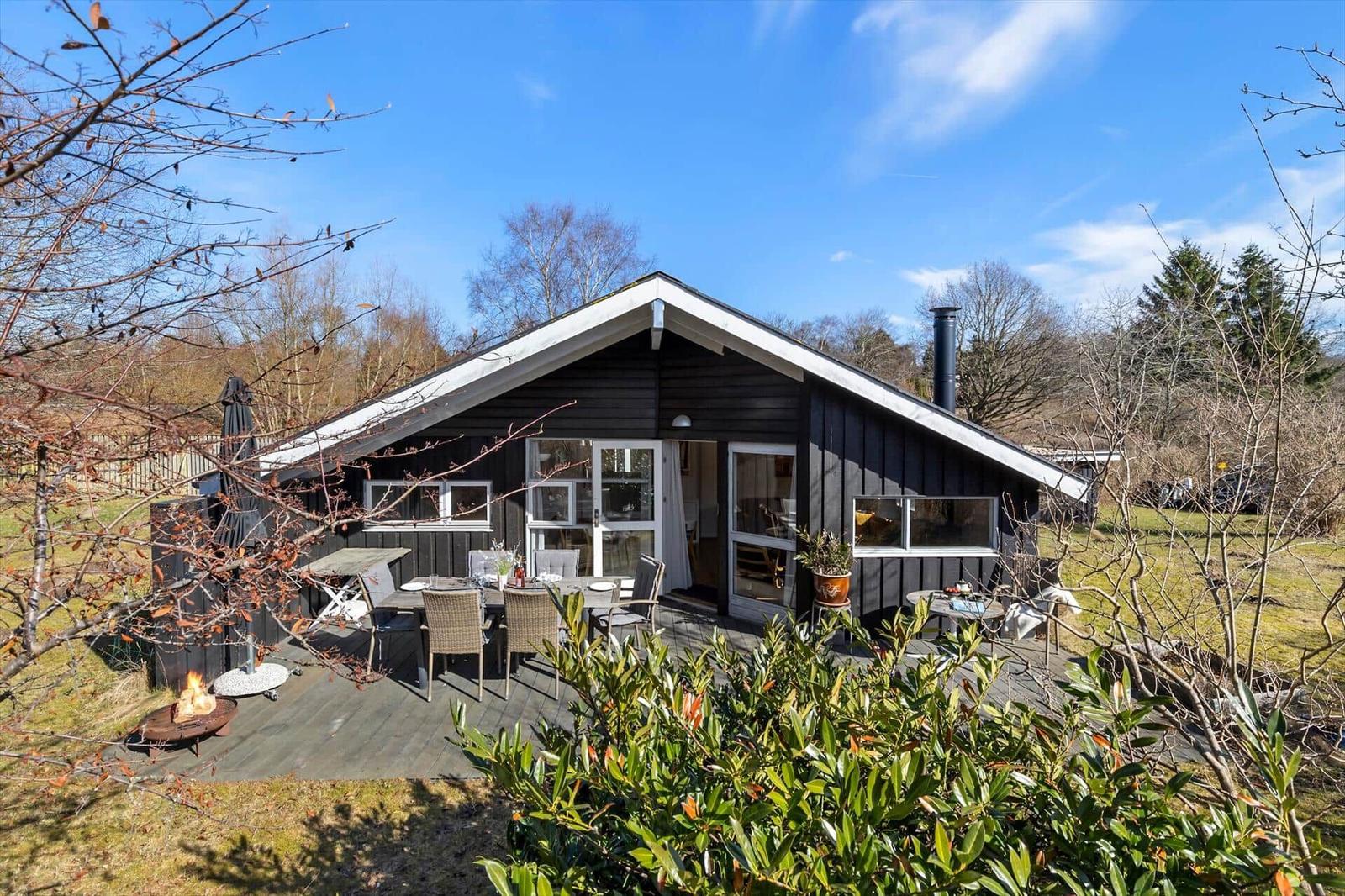 A dark wooden house with a terrace, grill, and outdoor seating.