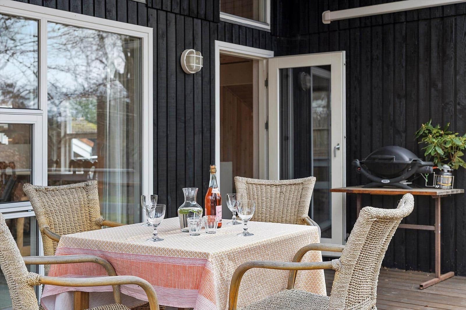 Terrace with table, chairs, and grill. Table set with bottle and glasses.