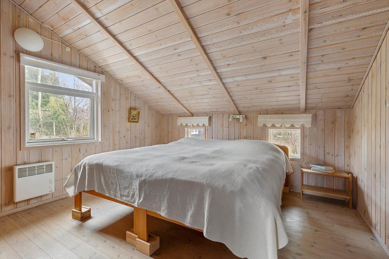 Bedroom with wooden walls and ceiling, large bed, windows, and heater.