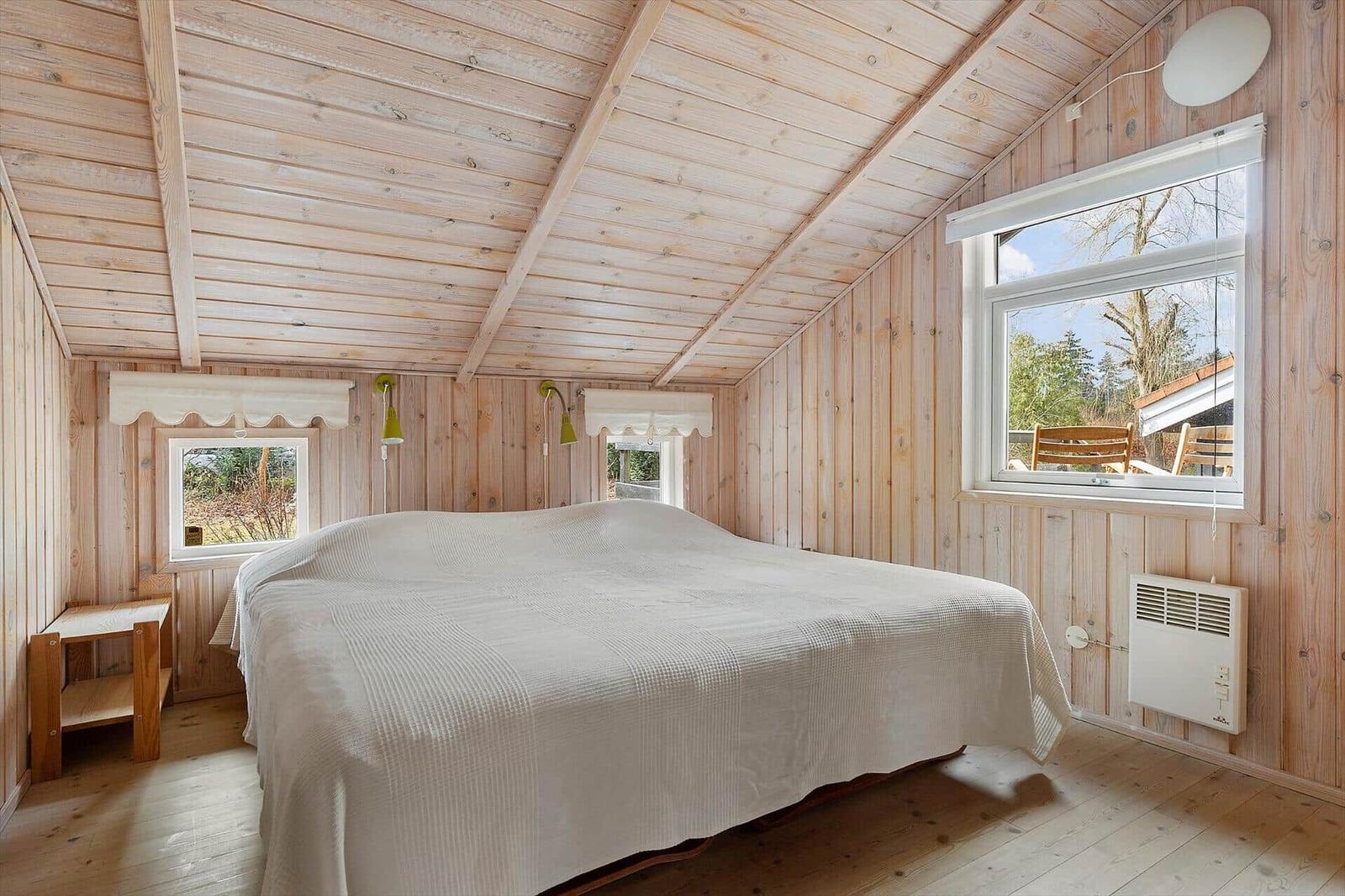 Bedroom with wooden walls and ceiling, large bed, windows overlooking garden.
