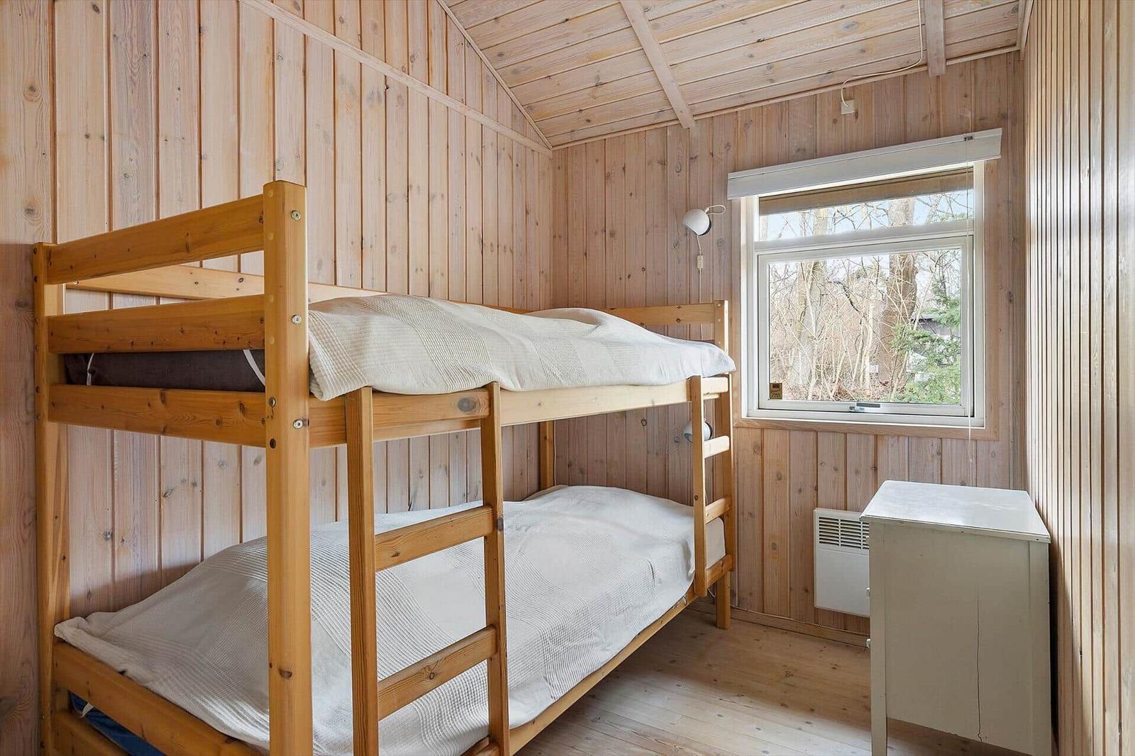 A bedroom with wooden walls and bunk bed. Window and dresser are visible.