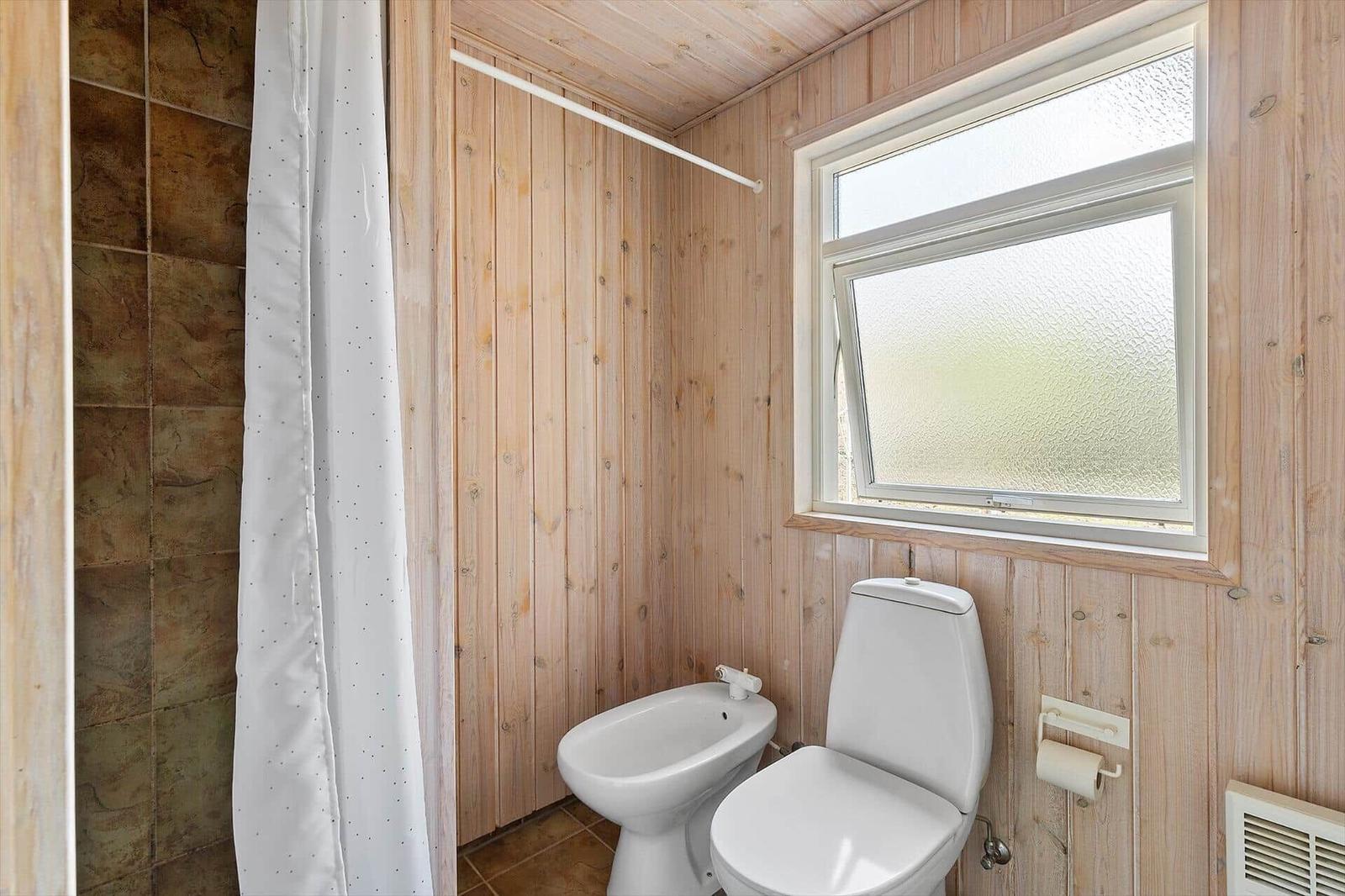 Bathroom with wooden walls, toilet, bidet, and shower with curtain.