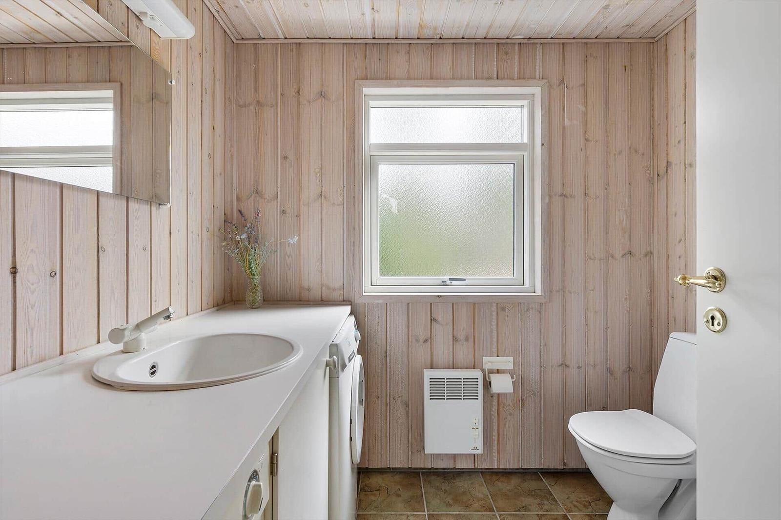 Bathroom with wooden walls, sink, toilet, and window.