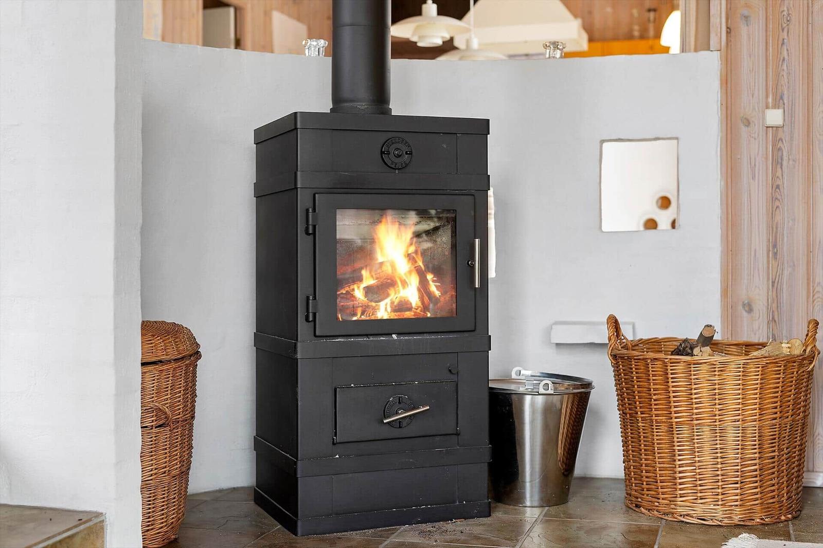 Black wood stove with burning fire, surrounded by baskets and a metal container.