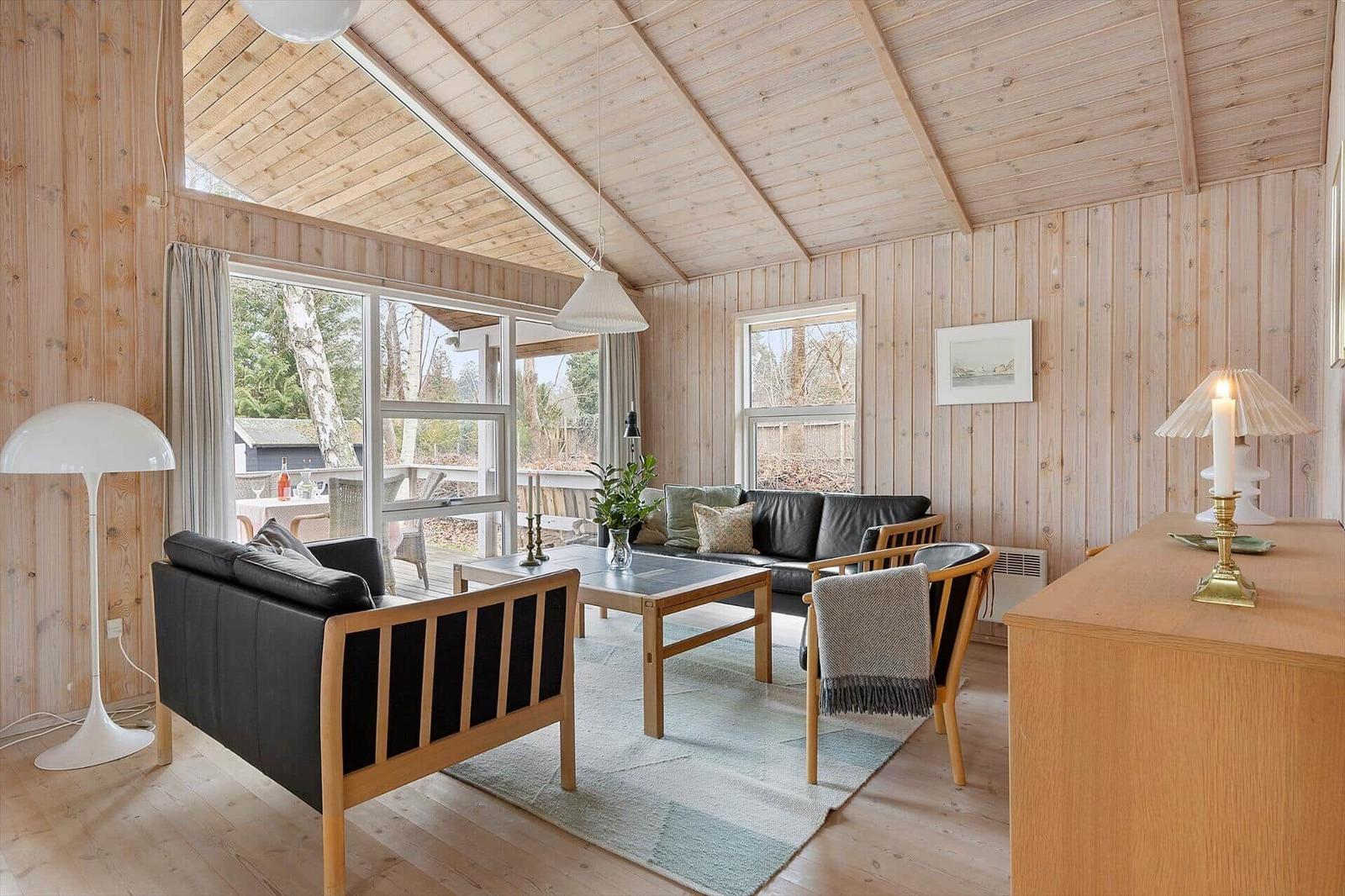 Living room with wooden walls, sofa, table, and windows to terrace.