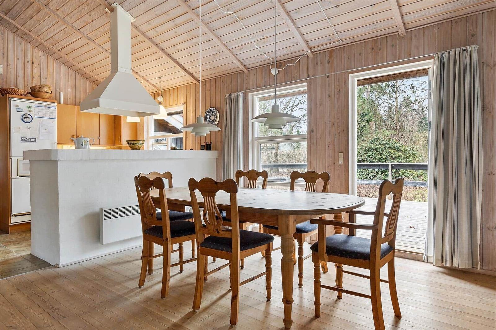Kitchen and dining area with wooden ceiling, table and chairs, windows to the terrace.