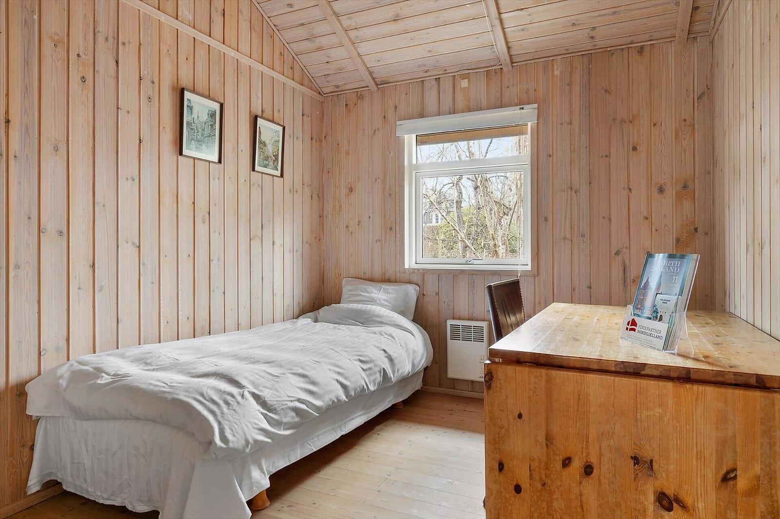 A bedroom with wooden walls, a bed, and a desk with a chair.