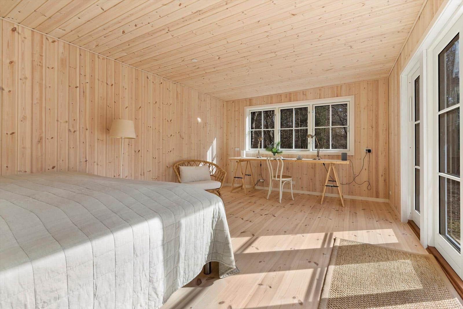 Bedroom with bed, desk, and window. Wooden walls and floor.