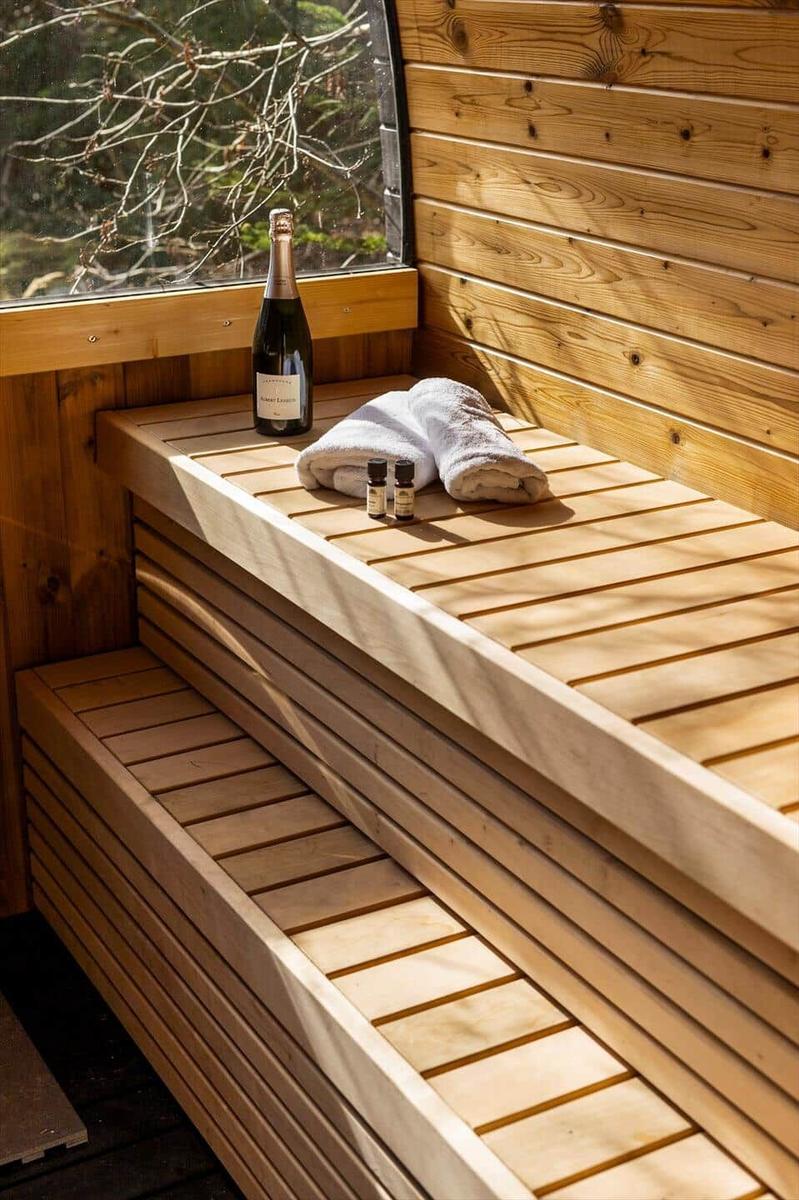 Wood sauna with bench, bottle, and towels. Window shows forest.