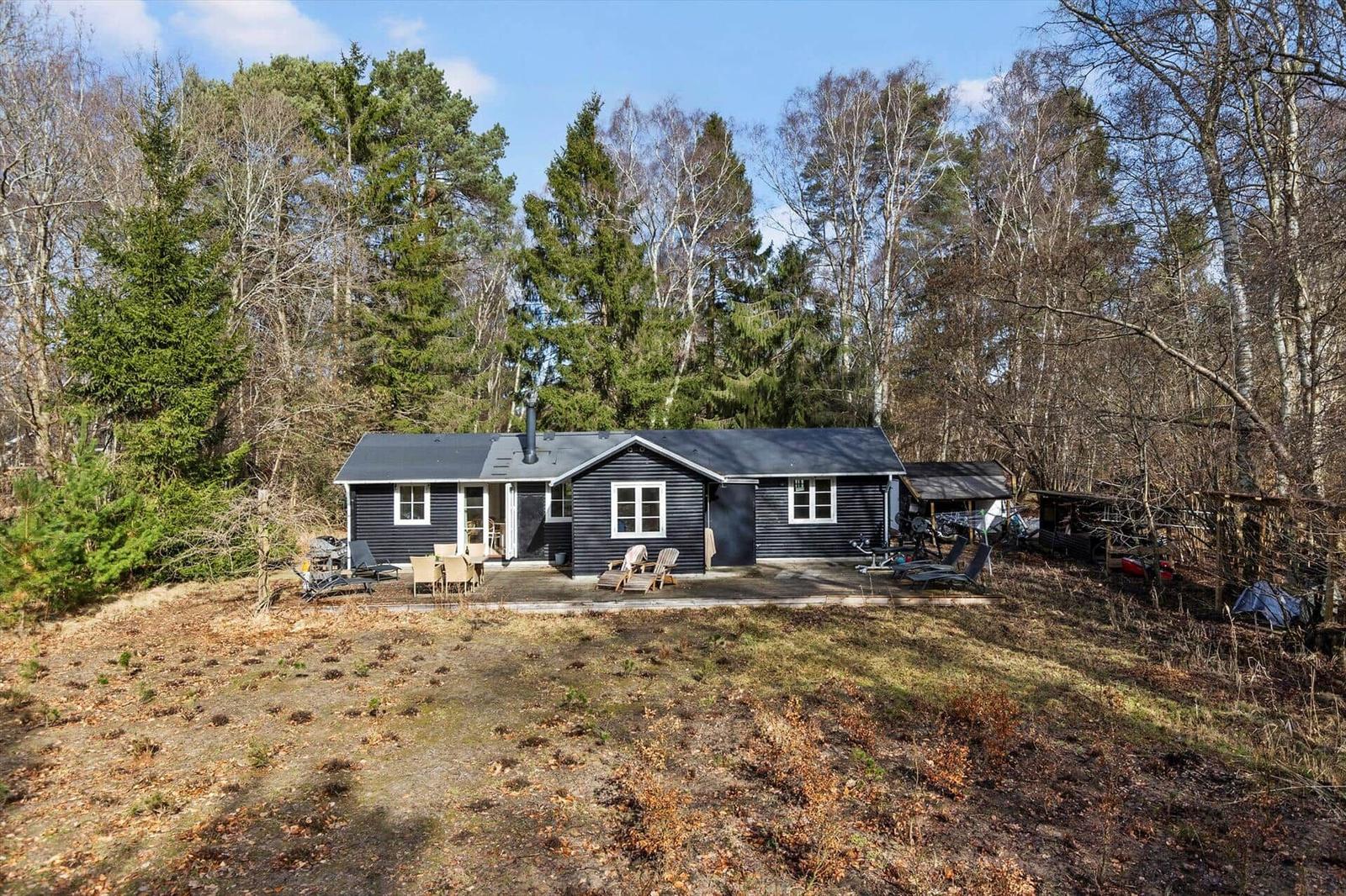 Black cabin with terrace in the woods. Garden area with lounge chairs.
