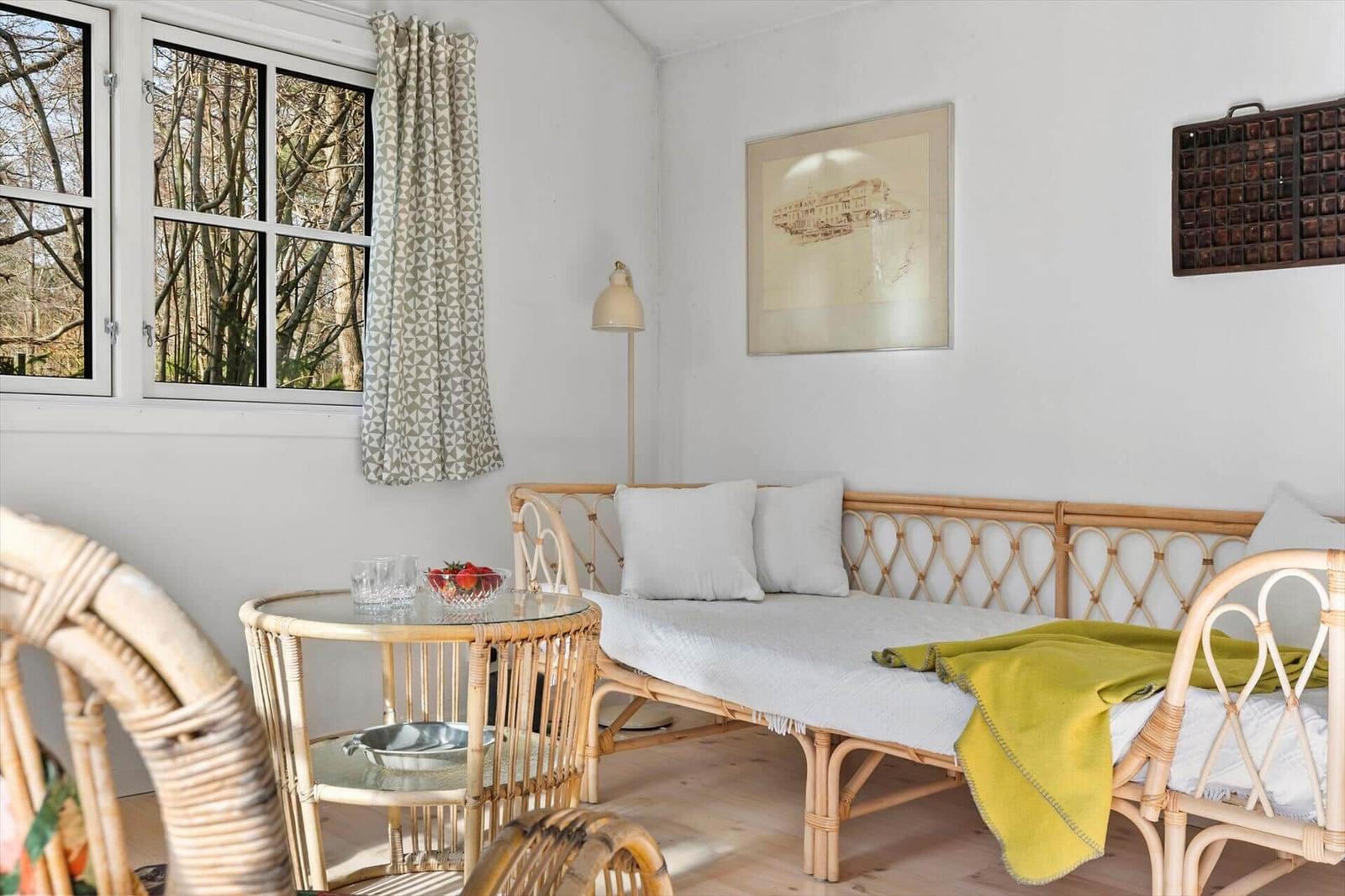 A room with rattan sofa, table, and window overlooking trees.