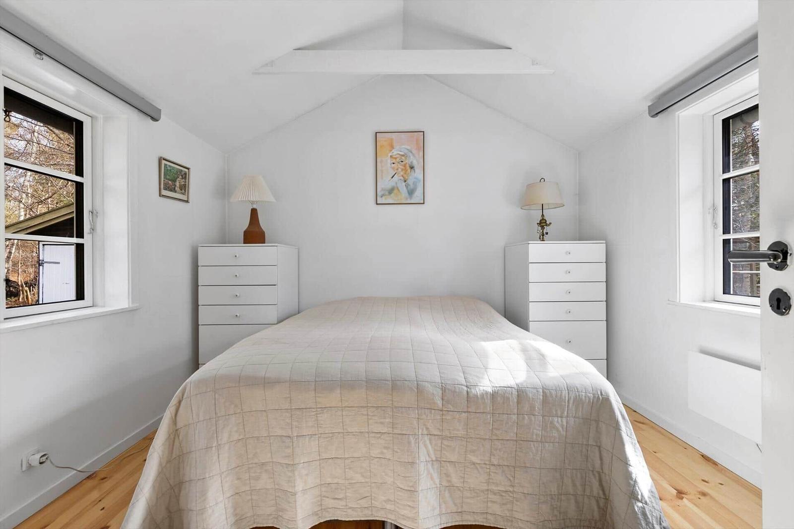 Bedroom with sloped ceiling, two windows, and a bed with white bedding.