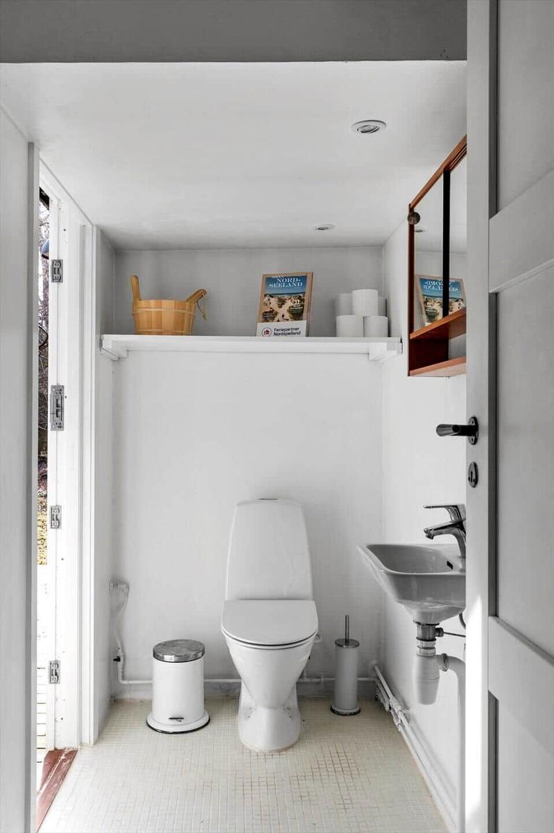 Bathroom with toilet, sink, and wooden bucket on shelf