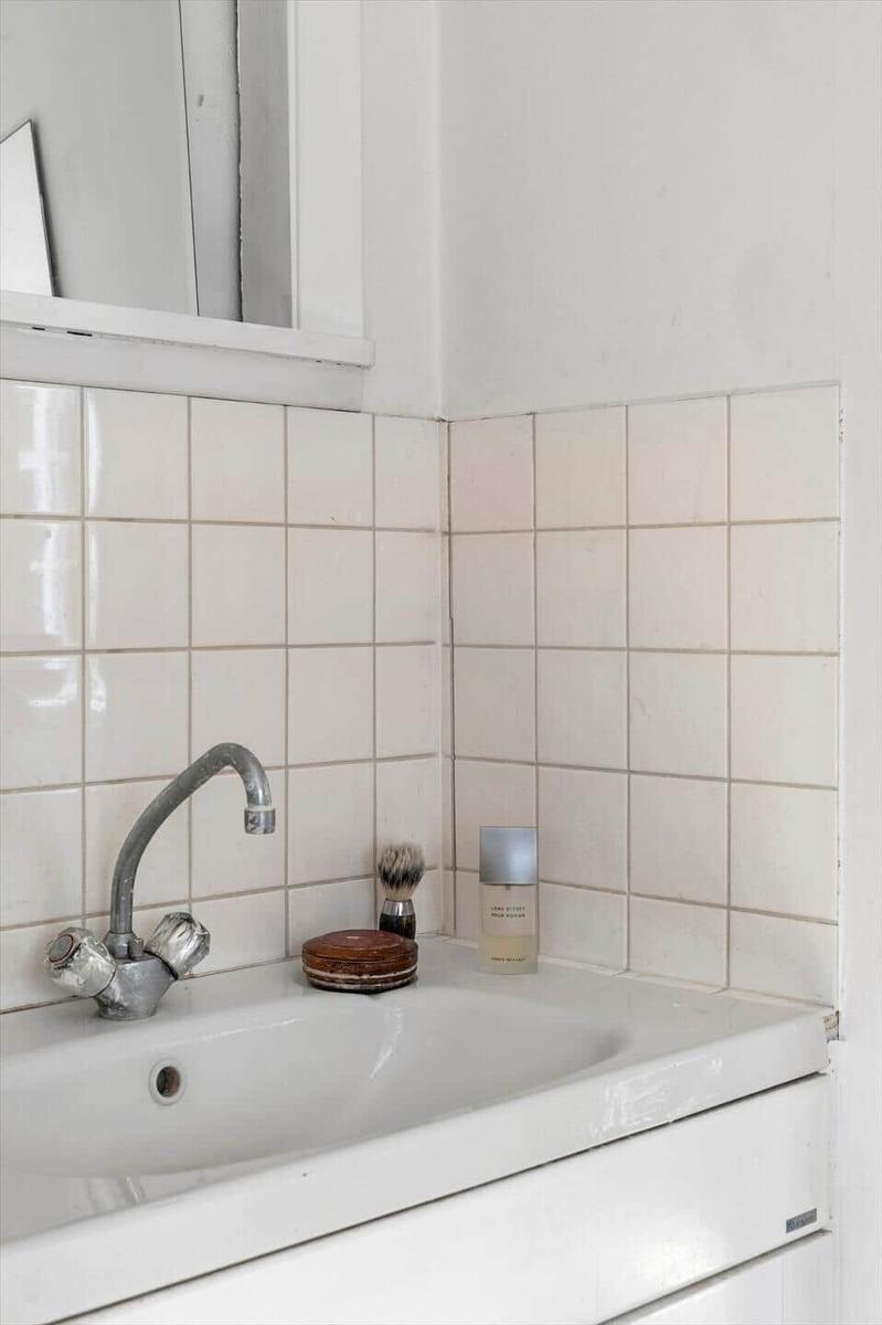 Sink with faucet and care items on white tiled wall