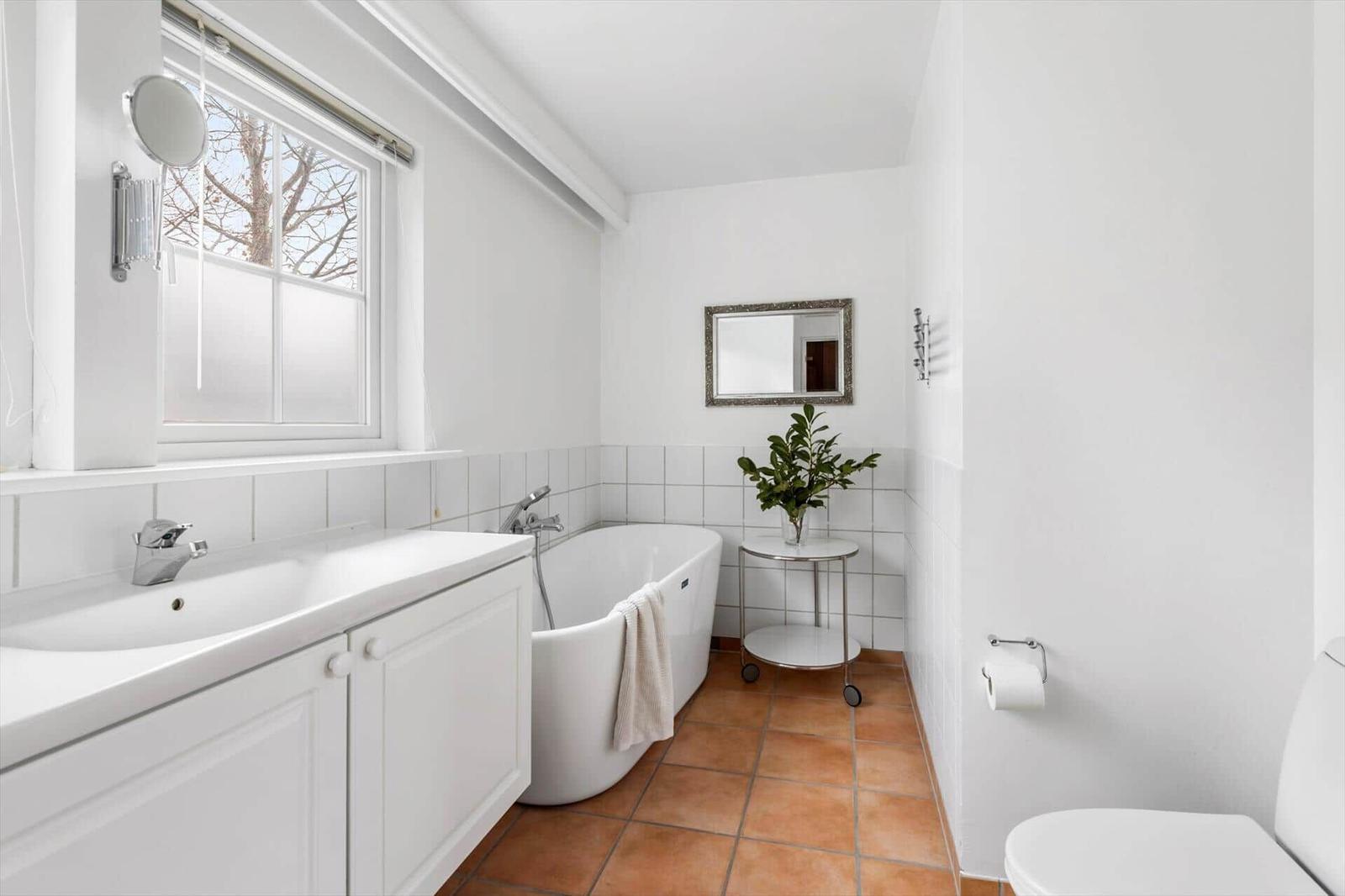 Bathroom with bathtub, sink, and toilet. Window, mirror, and plant visible.