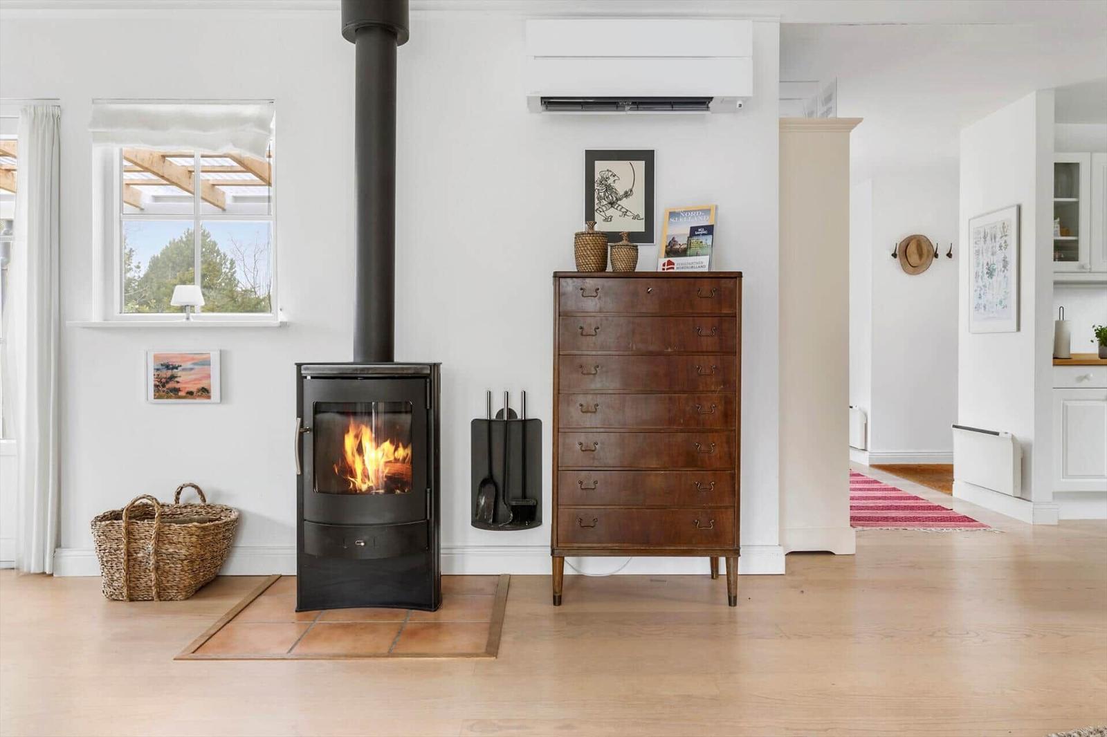 Wood-burning stove, wooden chest, and window with view to outdoors.