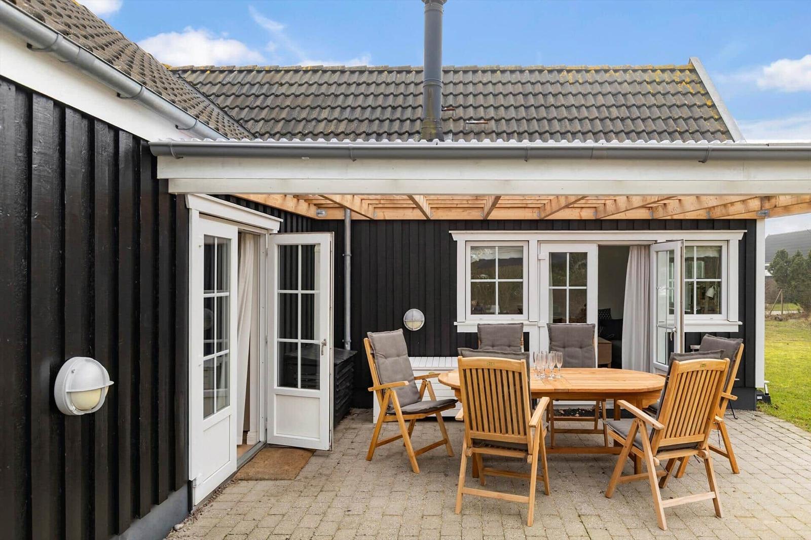 Terrace with wooden table and chairs, white doors, and black wooden house with roof.
