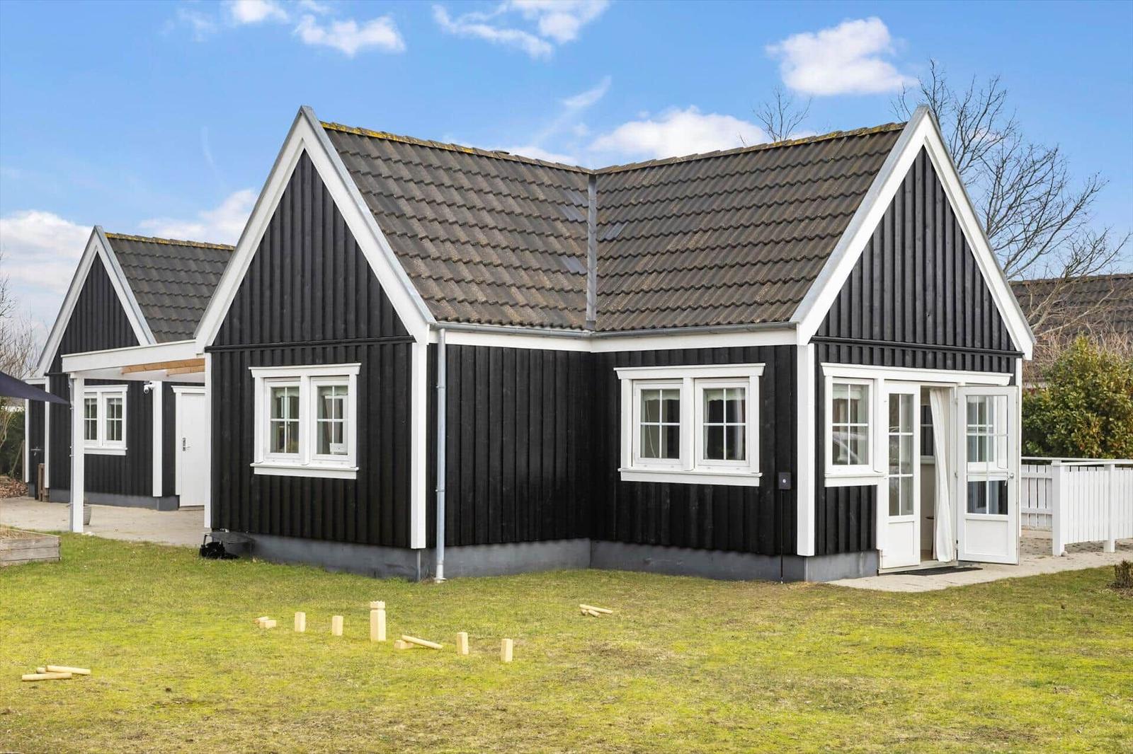 Black wooden house with white window frames and door, grassy area in front, clear sky.