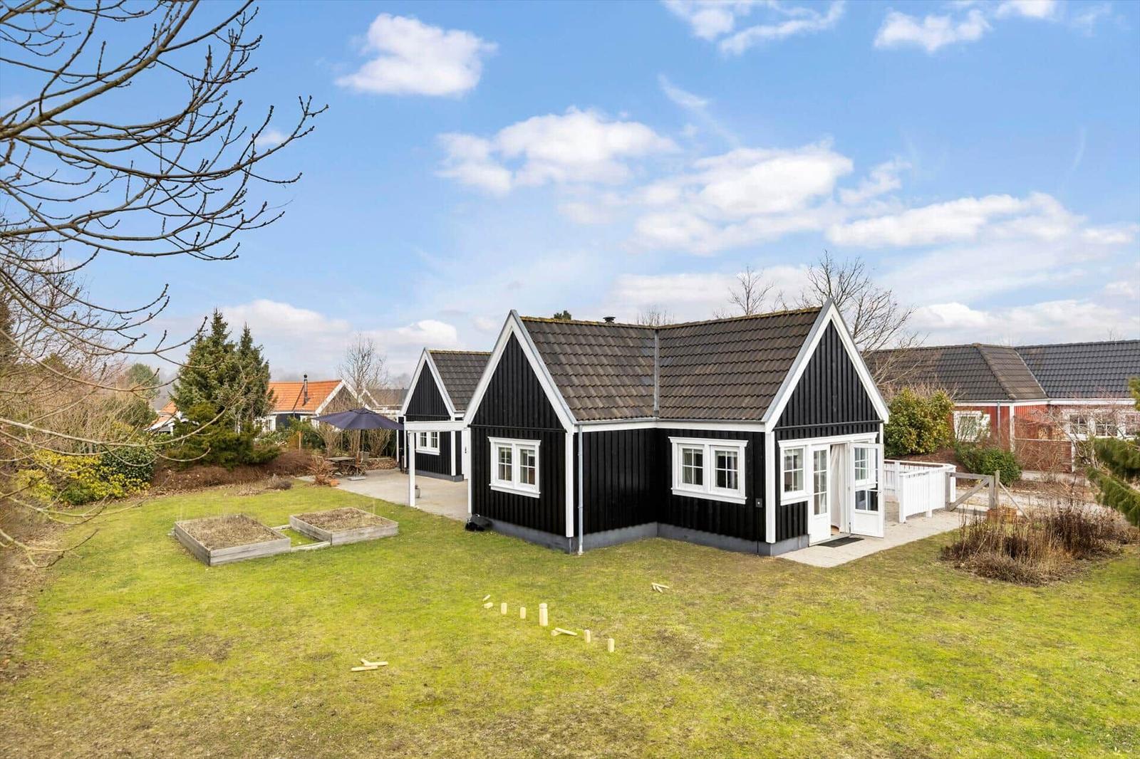 Black wooden house with white trim and garden. Backyard with terrace and umbrella.