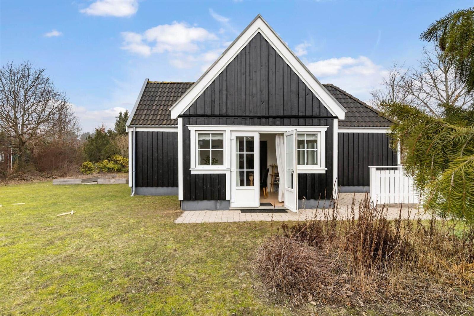 Black wooden house with white trim and open entrance. Lawn and trees in the background.