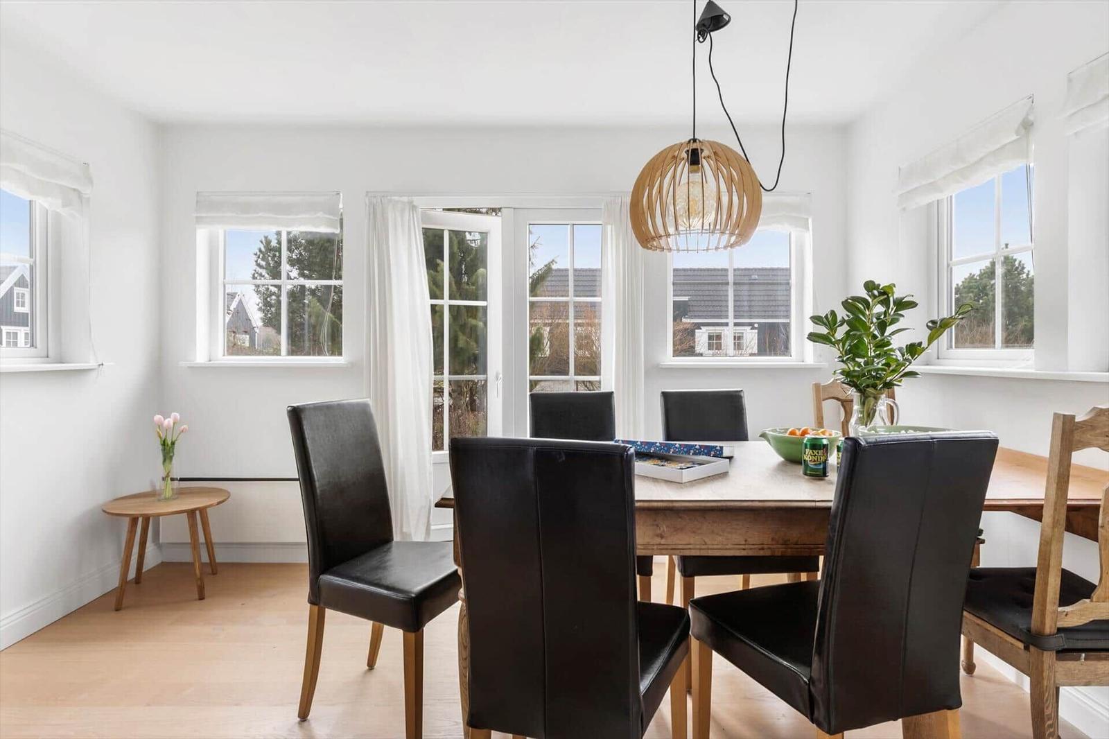 Dining room with wooden table, black chairs, and large windows.