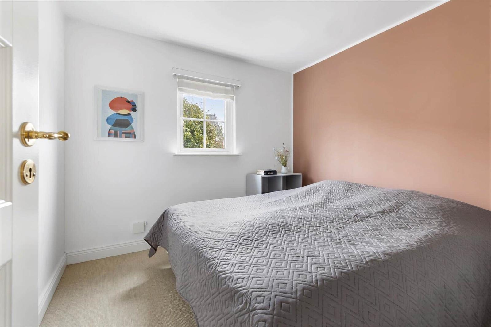 Bedroom with bed, window, and rose-toned wall.