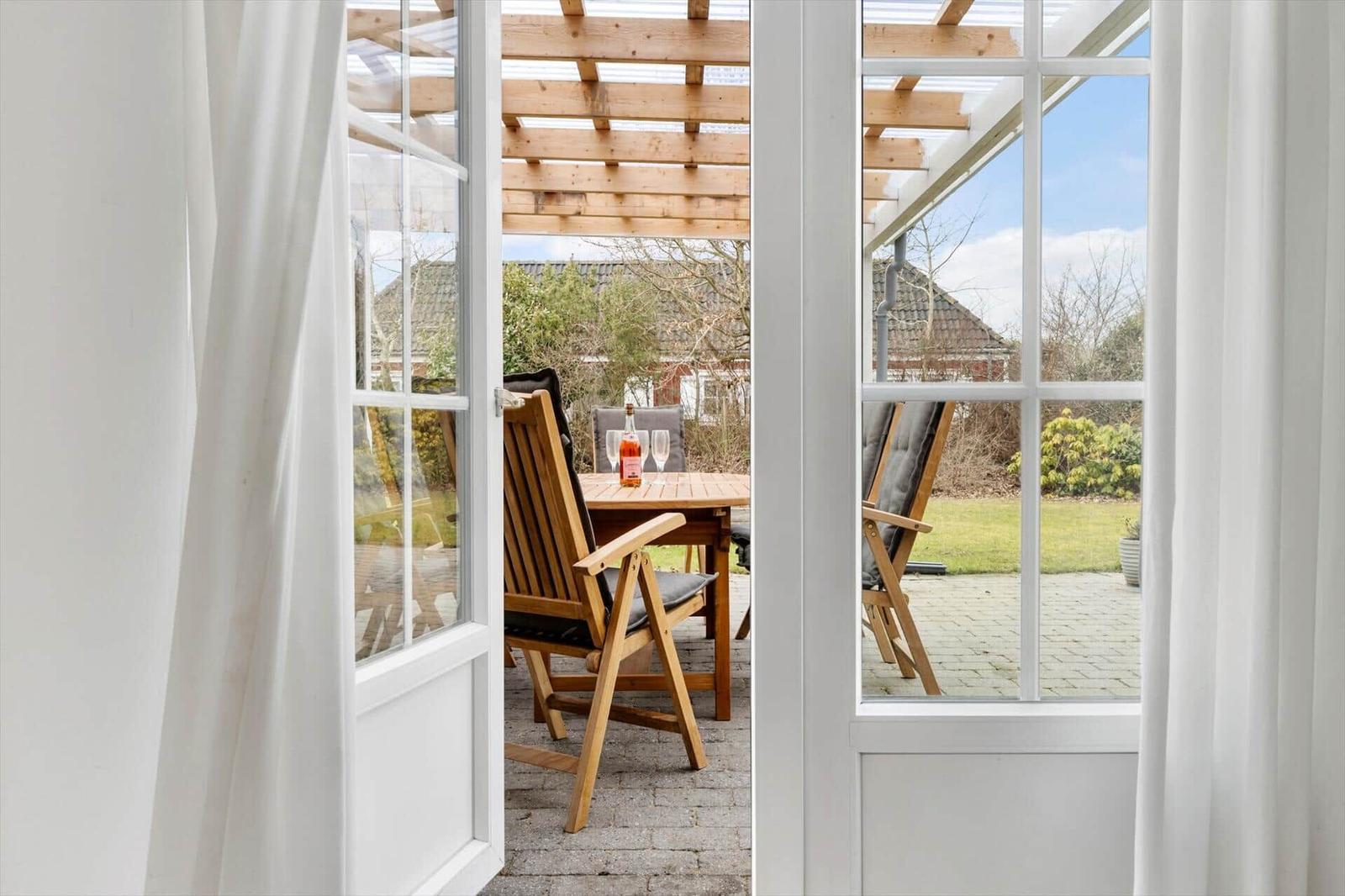 Through the glass door, a paved outdoor area with a wooden table, chairs, and a bottle is visible.