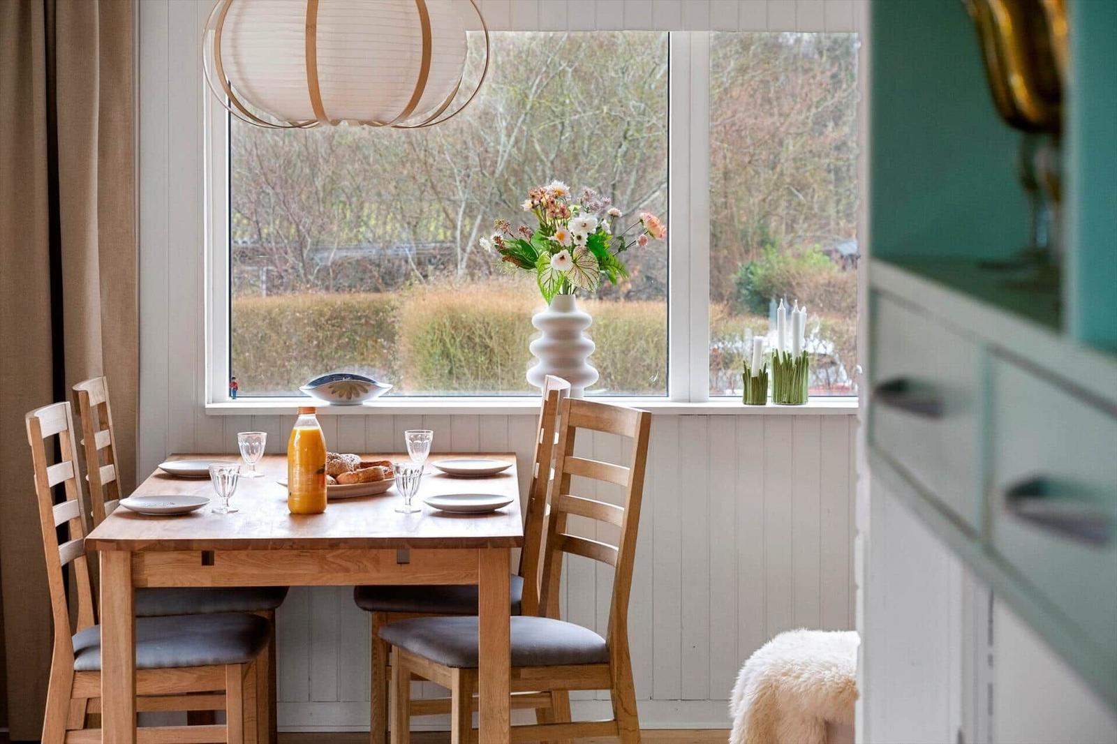 Dining table with chairs by window with flowers and landscape.