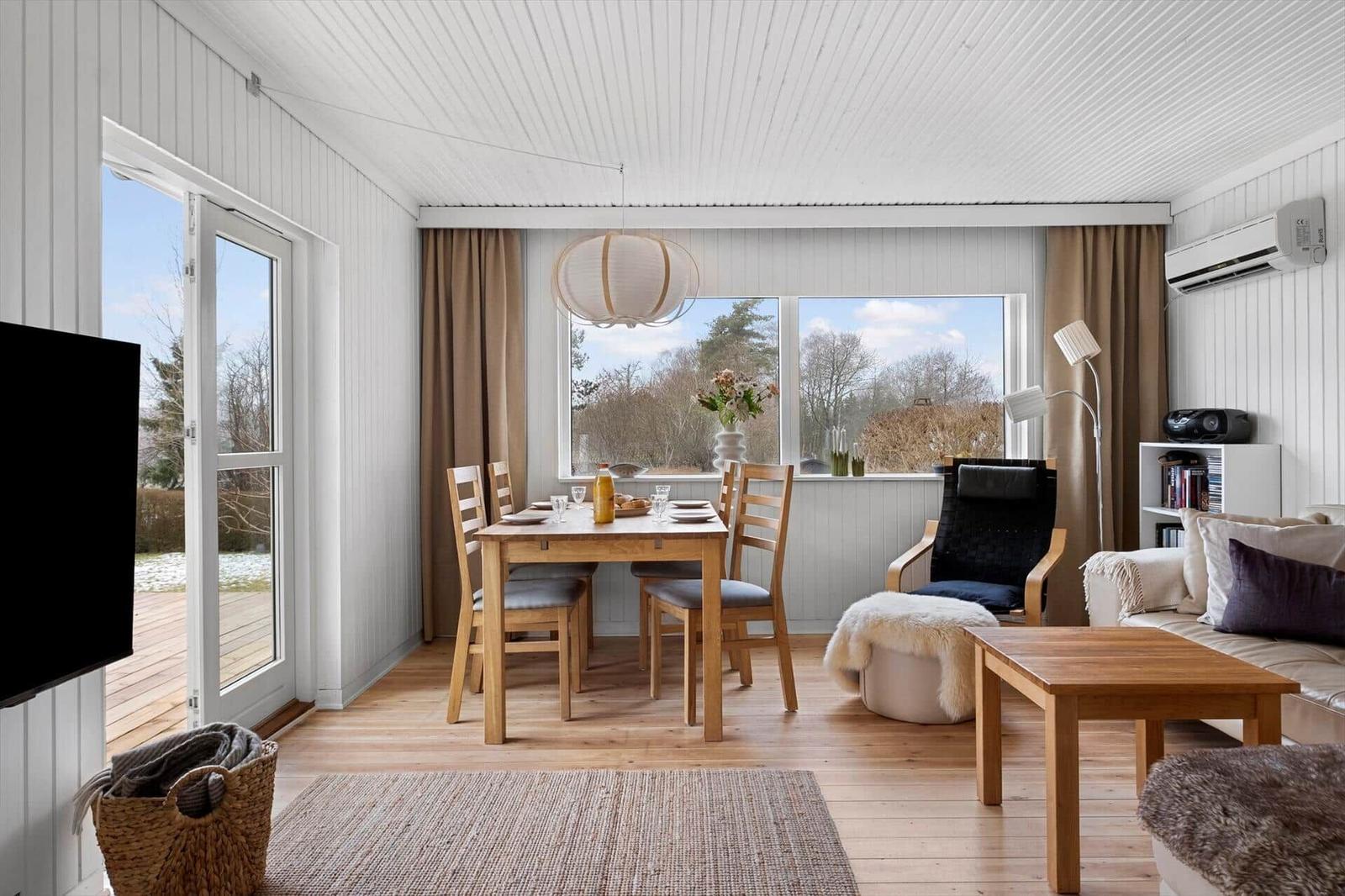 Living and dining area with wooden furniture, windows, and terrace door.