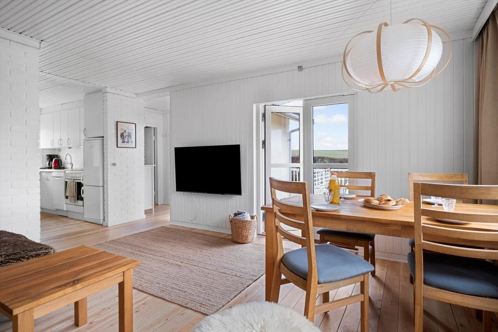 Living and dining area with wooden table, TV, and balcony view.