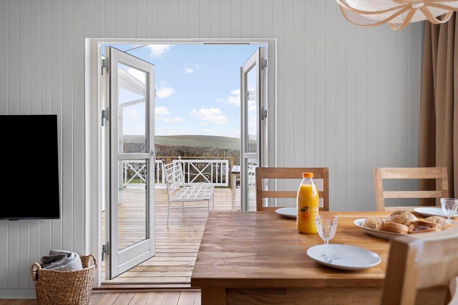 Dining area with table, chairs, and view of balcony overlooking landscape.