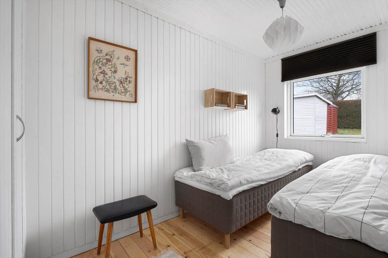 Two beds, wall art, wooden floor, and window with view outside.