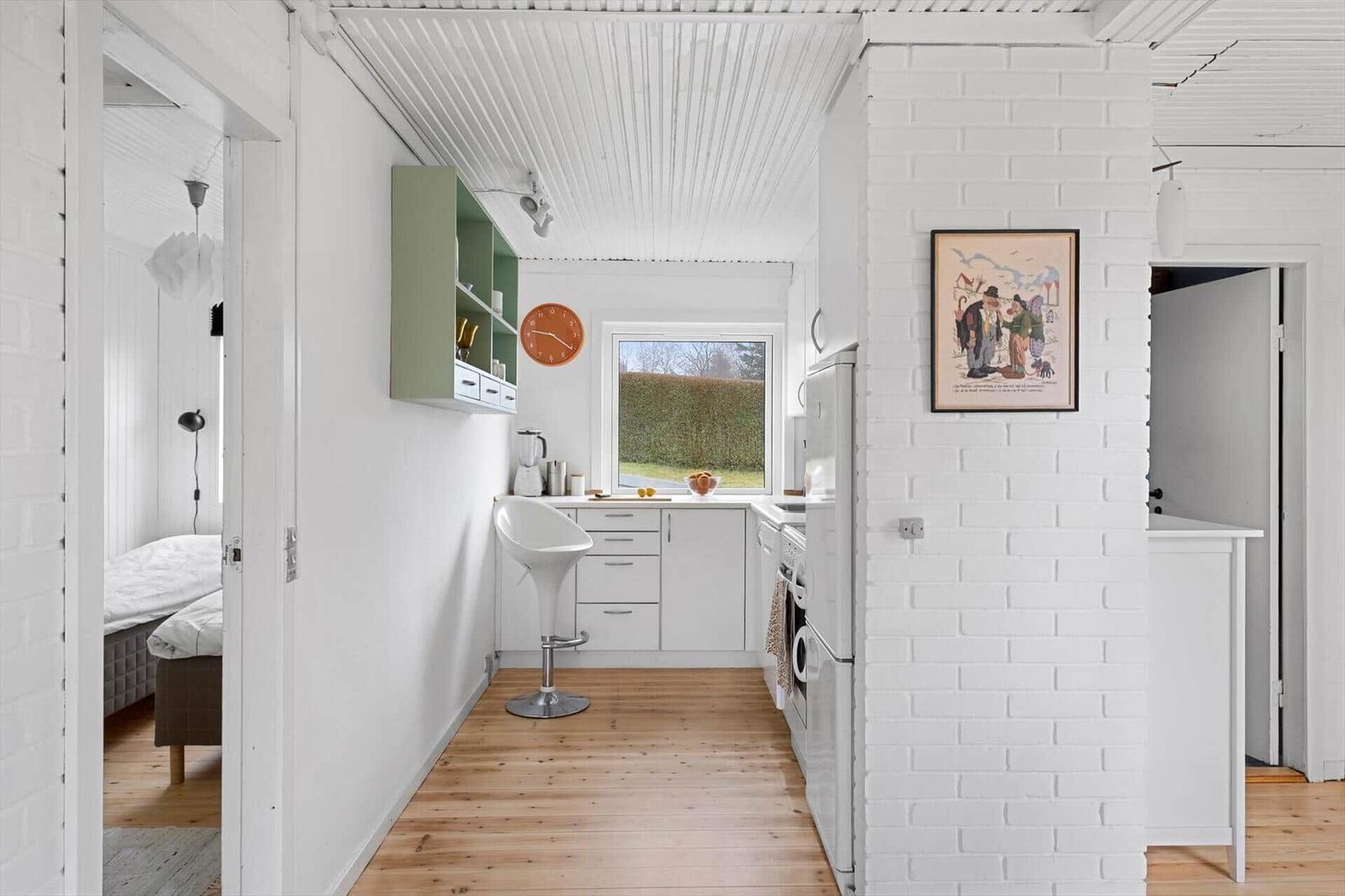 Kitchen with white cabinetry, wooden floor, and window. Left bedroom, right hallway.