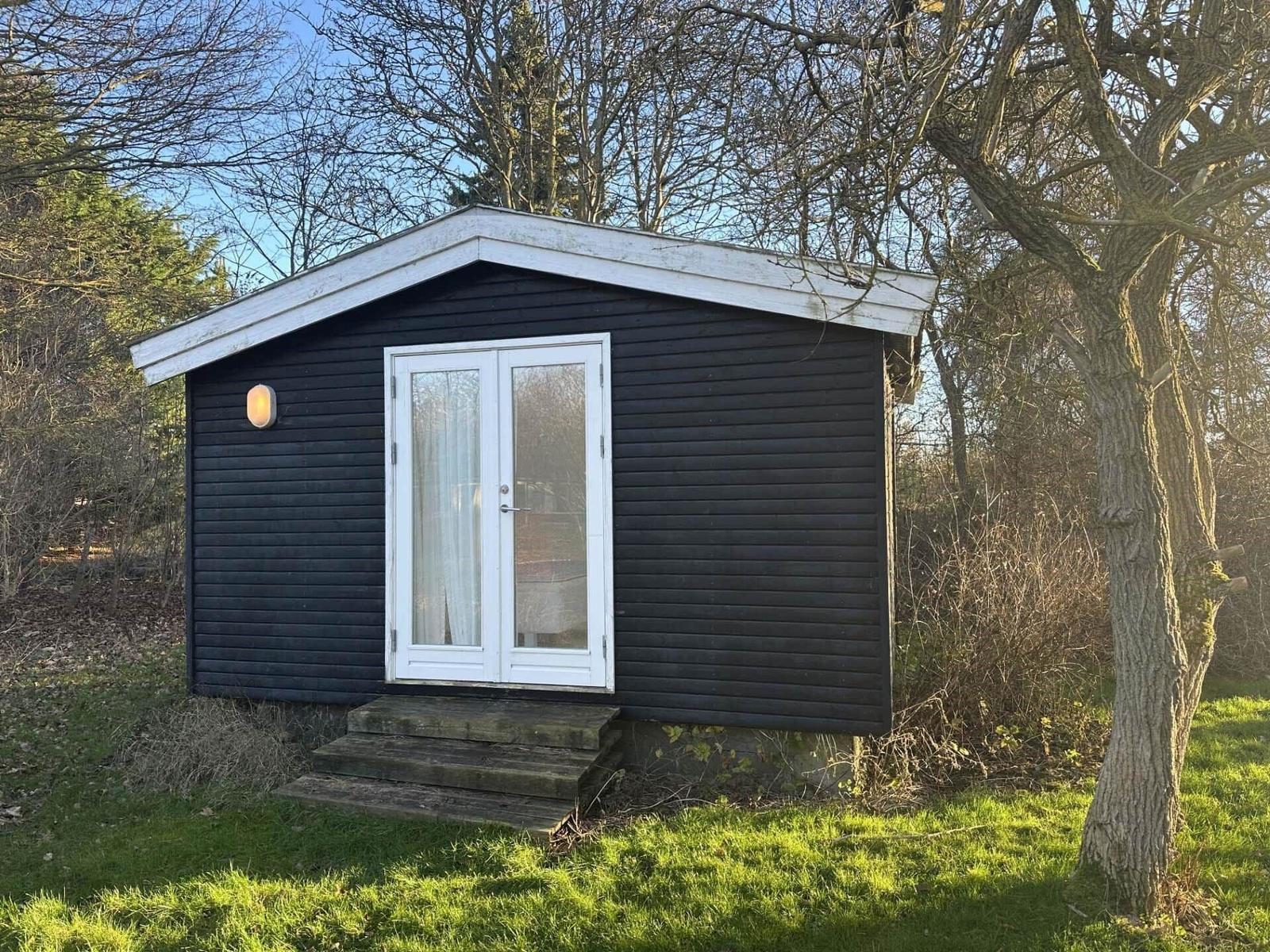 Black wooden cabin with white door and roof edge in the woods.