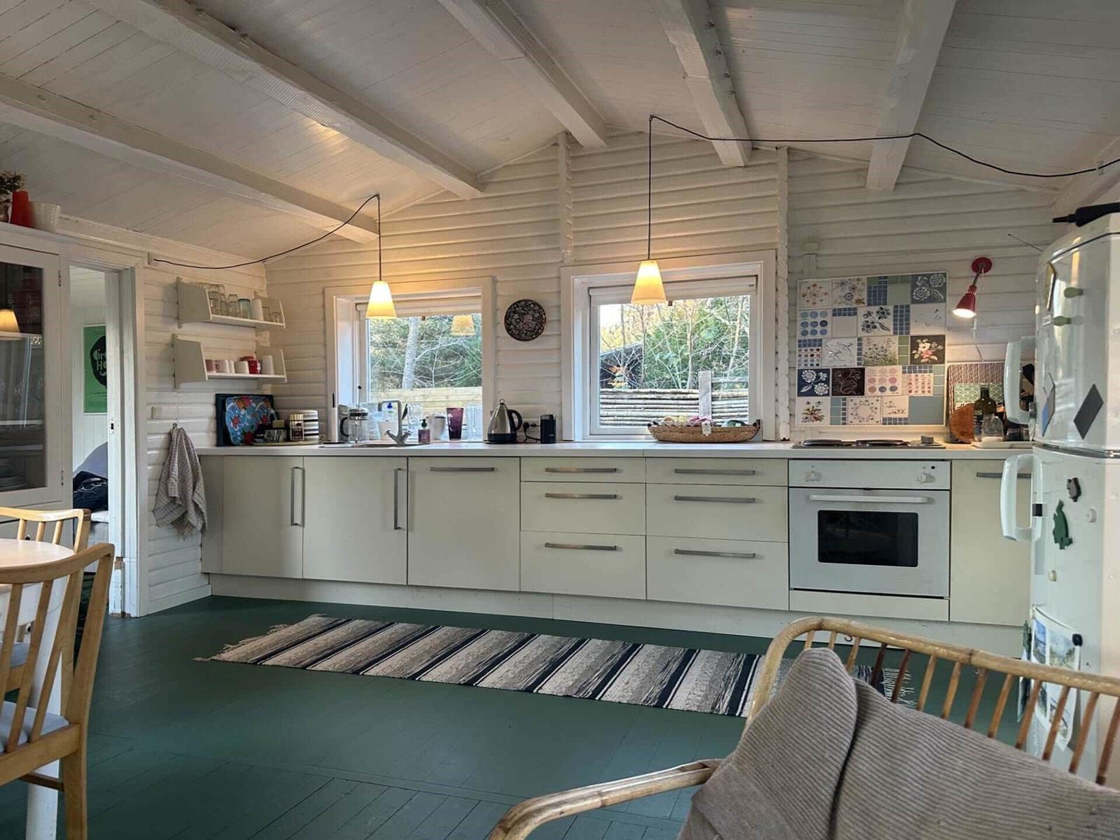 Kitchen with white cabinets, windows, and refrigerator. Wooden floor and rug.