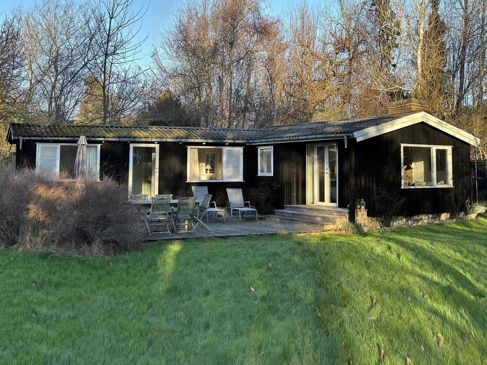 A dark wooden house with a terrace and garden. Multiple windows and doors are visible.